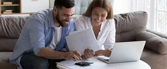 Happy couple sitting on a sofa, calculating their mortgage loan options together.