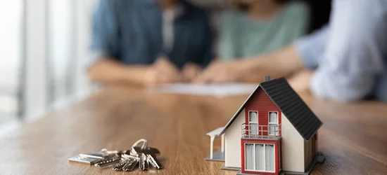Couple signing a mortgage contract behind a house replica, holding keys to their new home.